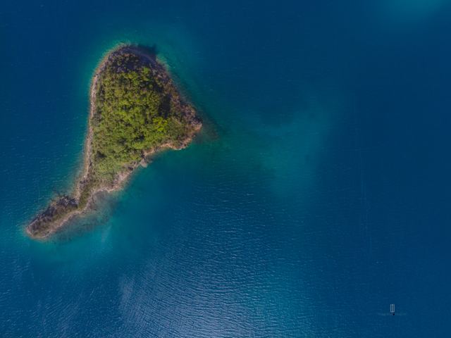 Islote cubierto de árboles en medio de una laguna azul, vista aérea