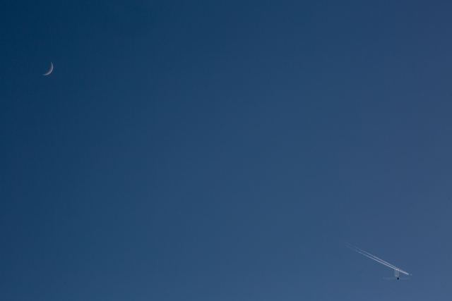 Luna creciente y la estela de un avión en el cielo